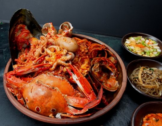 질그릇에 담은 붉은 양념 해물찜 — 꽃게·문어·홍합·소라·조개